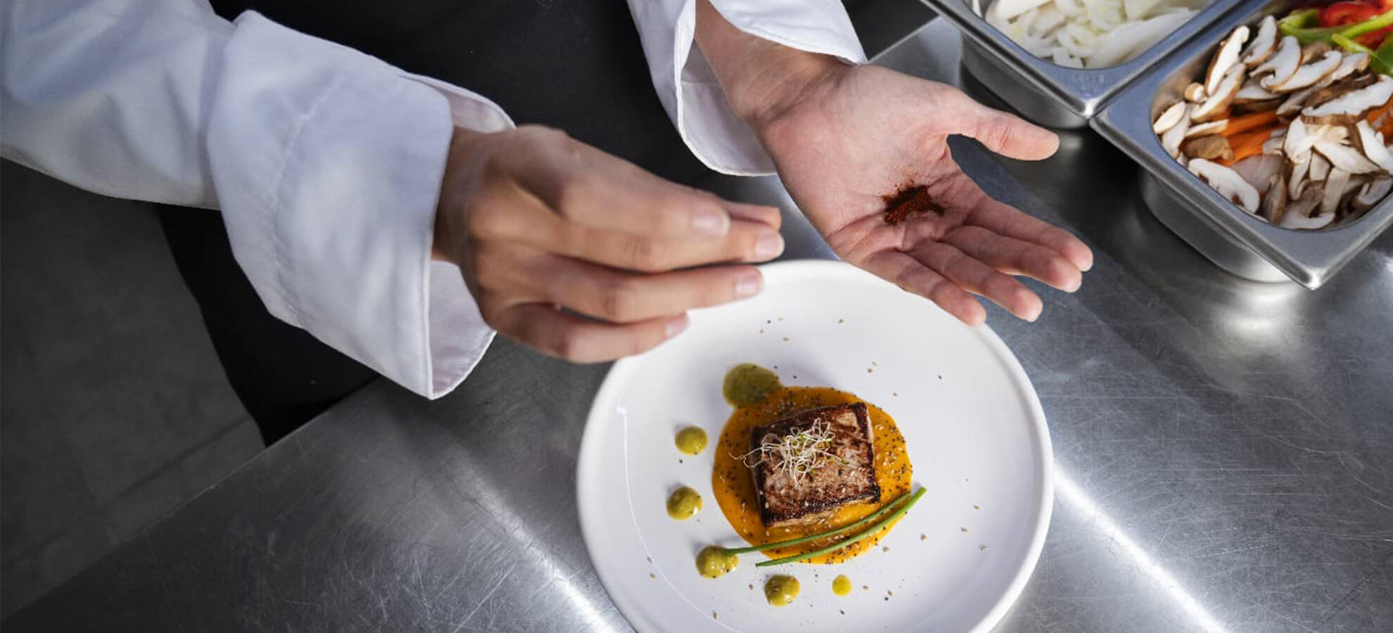 Chef garnishing a gourmet plated dish in a professional kitchen