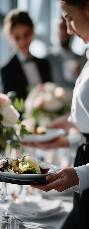 Server presenting plated gourmet dish at an elegant event table setting