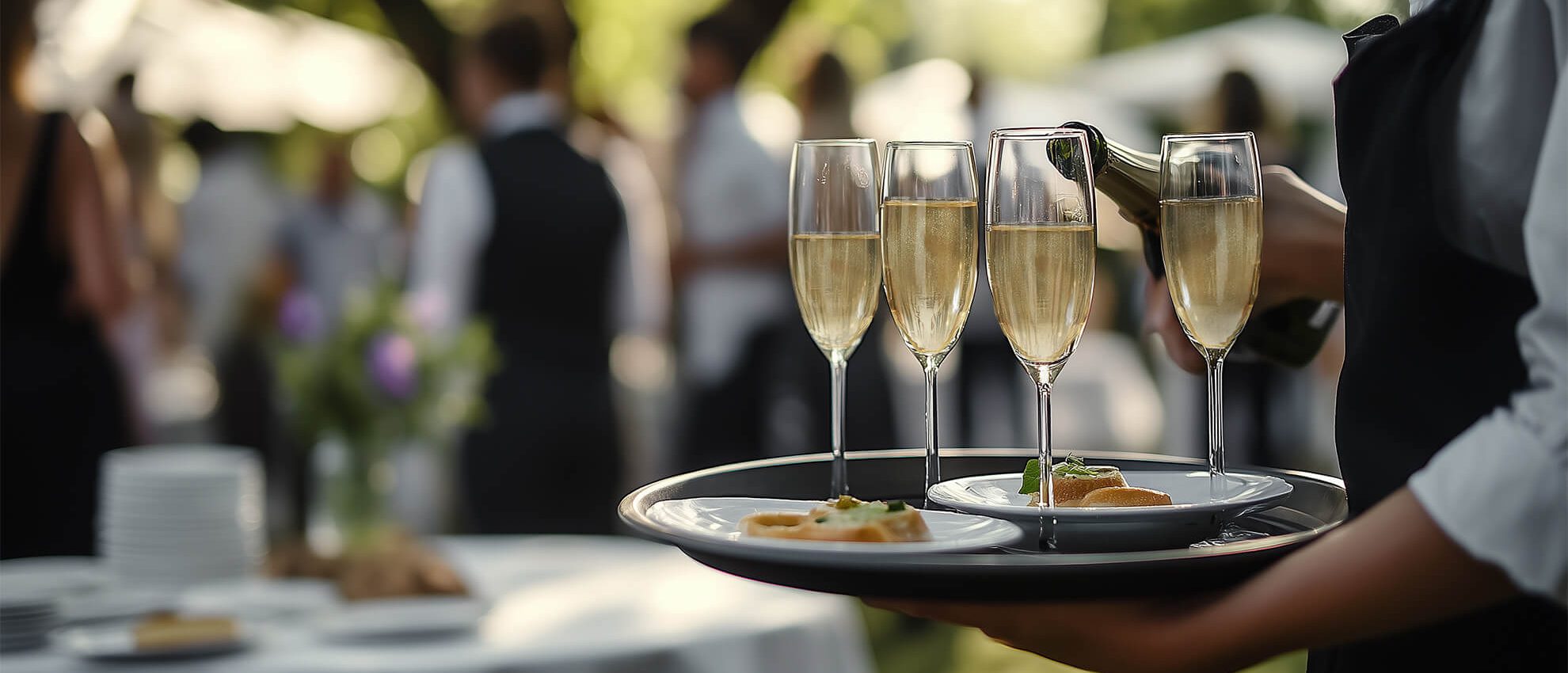 Waiter serving champagne glasses at an elegant outdoor social event with professional catering.