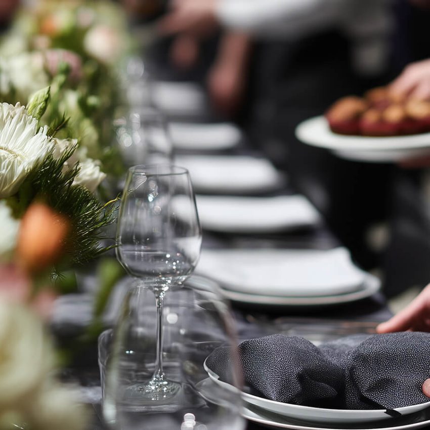 Server setting a beautifully decorated table with floral arrangements and glassware at an outdoor catered event